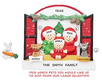 May include: A personalized Christmas ornament featuring a family of four standing in a window. The ornament is red, green, and white with a yellow frame. The family members are labeled "Dad", "Mom", and "Emily". The ornament also includes a dog and a cat, labeled "Aspen" and "Patches". The text "The Smith Family" is printed below the window. The ornament is a customizable option for families to add their own pets.