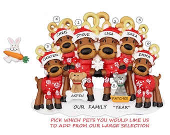 May include: A Christmas ornament featuring a family of six reindeer wearing red and white sweaters with snowflakes. The reindeer are arranged in a circle with their names written on their hats: Chris, Steve, Lisa, Sara, Carter, and Emma. The ornament also includes two pets: a dog named Aspen and a cat named Patches. The text "Our Family" and "Year" is also included on the ornament.