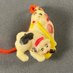 May include: A white and black charm with a red and yellow design. The charm is shaped like two dogs, one on top of the other. The charm is attached to a red string.
