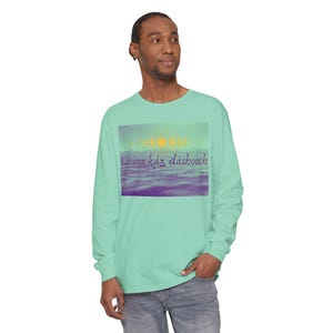 May include: A turquoise long-sleeve t-shirt with a graphic of a sunset over a purple and blue ocean. The graphic includes the text "Iatseen Kâx dashbooch" and "Drinking for Strength".