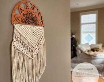 May include: Beige macrame wall hanging with a wooden half-circle top featuring a mandala design. The text "Melled it" is visible in the lower right corner of the image. The text "Handmade macrame art and decor" is visible below the text "Melled it". The text "Style pictured: Mandala D, Color Beige" is visible at the bottom of the image.