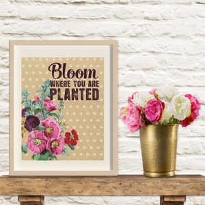 May include: A framed print with a burlap background and white polka dots. The print features a floral design with pink and purple flowers and the text "Bloom where you are planted".