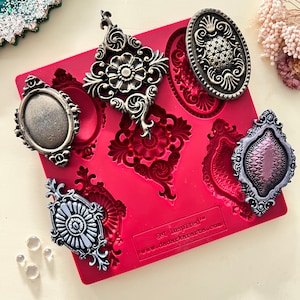 Könnte beinhalten: Eine rote Silikonform mit sechs verschiedenen verzierten Designs. Die Designs sind in Form eines Rahmens, einer Blume und eines Wirbels. Die Form ist mit "Get Inspired™" und "www.dadarkarts.com" beschriftet.