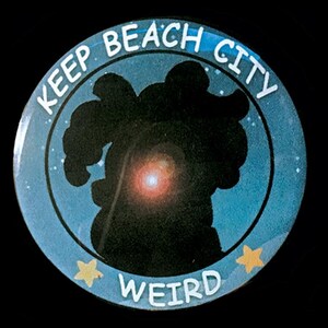 May include: A blue and white button with the text "Keep Beach City Weird" in white lettering. The button features a silhouette of a character with a red glow in the center.