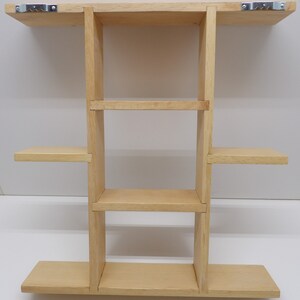 Puede incluir: Una estanter&iacute;a de pared de madera clara con cuatro estantes. La estanter&iacute;a est&aacute; fijada a la pared con dos soportes met&aacute;licos.