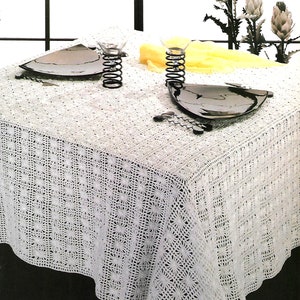 May include: White crocheted tablecloth with a delicate floral pattern. Two black plates and two metal candle holders are placed on the tablecloth.