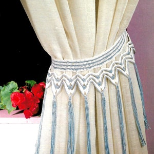 Peut inclure: Rideaux blancs en voile avec une bordure en crochet et des glands bleus. La bordure est un motif délicat avec un bord festonné.