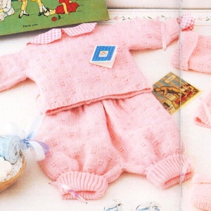 May include: A pink knitted baby outfit with a gingham collar and matching booties. The outfit includes a sweater, trousers, and booties.