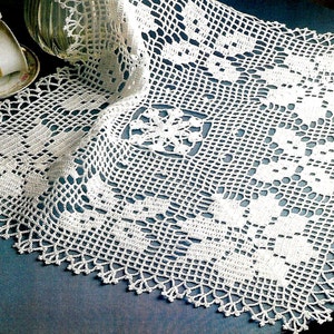 May include: White crocheted table runner with a delicate floral pattern. The runner has a scalloped edge and is made with a fine thread.