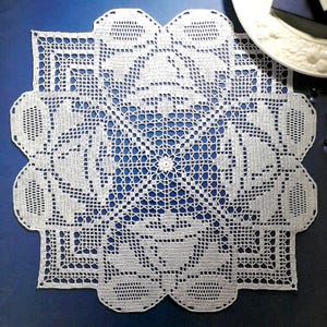 May include: White crocheted doily with a square center and intricate floral designs around the edges.