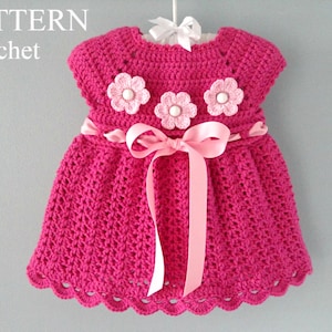 May include: A pink crocheted baby dress with a pink ribbon sash and three pink and white crocheted flowers.