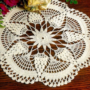May include: A white crocheted doily with a delicate floral design. The doily is circular and has a scalloped edge.