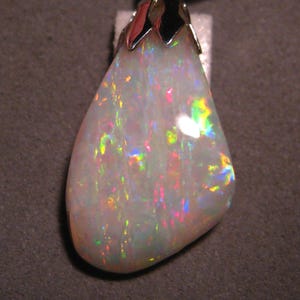 May include: A teardrop-shaped opal pendant with a silver setting. The opal has a white base with iridescent flashes of blue, green, and pink.
