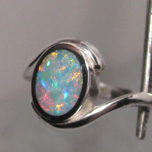 May include: A silver ring with an oval opal gemstone. The opal exhibits a vibrant play of colour with blue, green, and red hues. The ring's band has a smooth, curved design.
