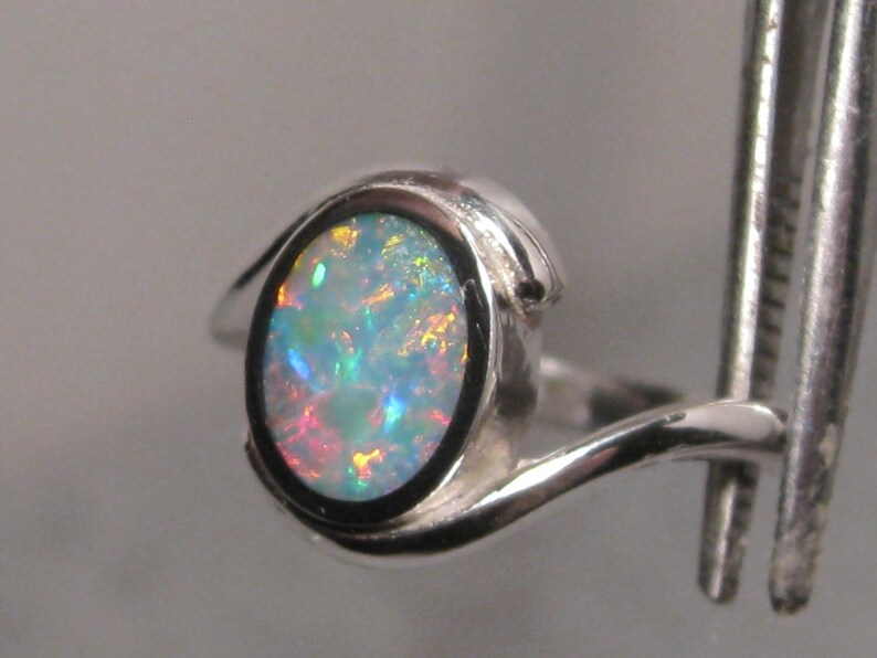 May include: A silver ring with an oval opal gemstone. The opal exhibits a vibrant play of colour with blue, green, and red hues. The ring's band has a smooth, curved design.