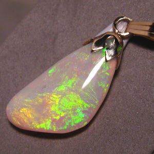 May include: A pear-shaped opal pendant with a gold bail. The opal displays vibrant flashes of green, yellow, and pink hues. The pendant is set in a gold setting, showcasing the gemstone's natural beauty. A unique piece of jewelry.