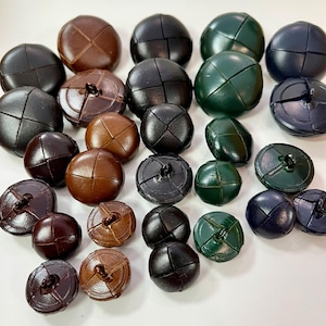 May include: A selection of leather buttons in a variety of colours, including brown, black, green and blue. The buttons feature a distinctive stitched design and are ideal for adding a handmade touch to clothing or crafts.