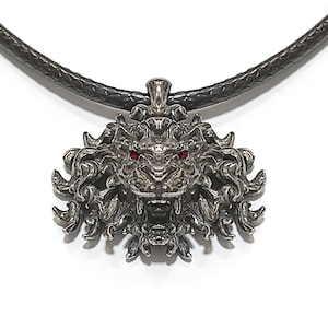 May include: A silver lion head pendant with red eyes, attached to a black leather cord necklace.