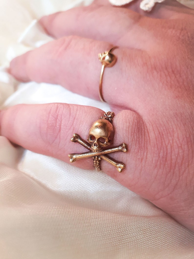 May include: A gold skull and crossbones ring. The ring is worn on a finger.