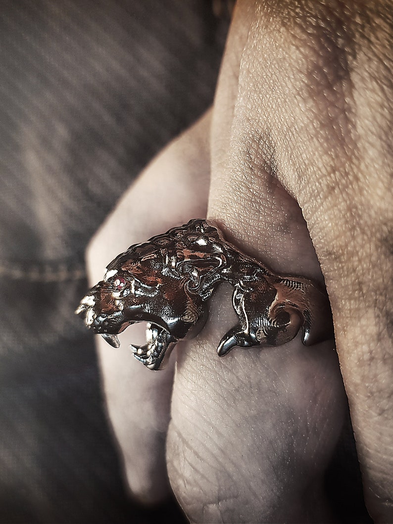 May include: A silver ring with a detailed design of a snarling panther with red eyes.