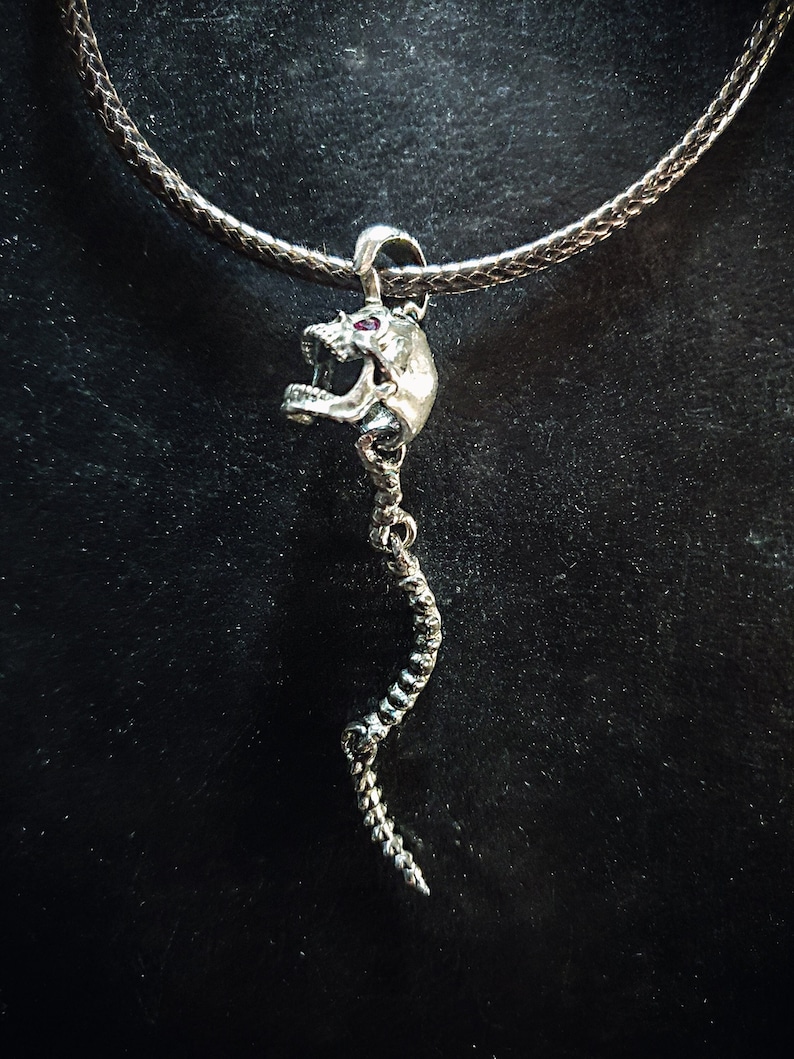 May include: Silver skull pendant necklace with a long, twisted, snake-like chain. The skull has red eyes.
