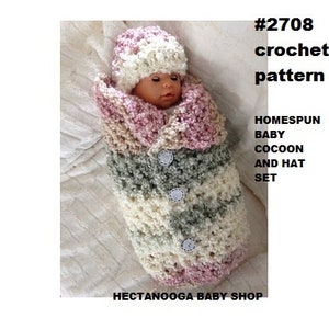 May include: Crochet pattern #2708 for a Homespun Baby Cocoon and Hat Set. The set is made in pink, cream, and green yarn and features a crocheted hat with a pom-pom.