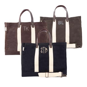 May include: Three canvas tote bags in brown and navy blue, each with a cream-coloured stripe down the centre. The bags have leather handles and are personalised with initials. One bag has a detachable shoulder strap.