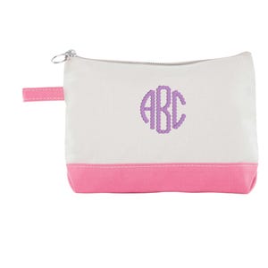 May include: A white canvas cosmetic bag with a pink bottom and a matching pink handle. The bag features a silver zipper and a purple embroidered monogram of the letters "ABC".