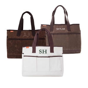 May include: Three tote bags in the image. Two are brown with dark brown handles and pockets, and the third is white with brown trim and handles. The brown bags have initials "AJ" and "SKYLAR" embroidered on them. The white bag has the initials "SH".