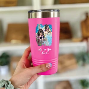 May include: A bright pink stainless steel tumbler with a silver rim and a lid. The front features a printed graphic of two children wearing sunglasses in a swimming pool, with the white cursive text "We Love You Mom!" printed below.