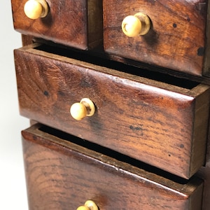 May include: A small wooden chest with four drawers. Each drawer has a bone knob and is made of dark wood.