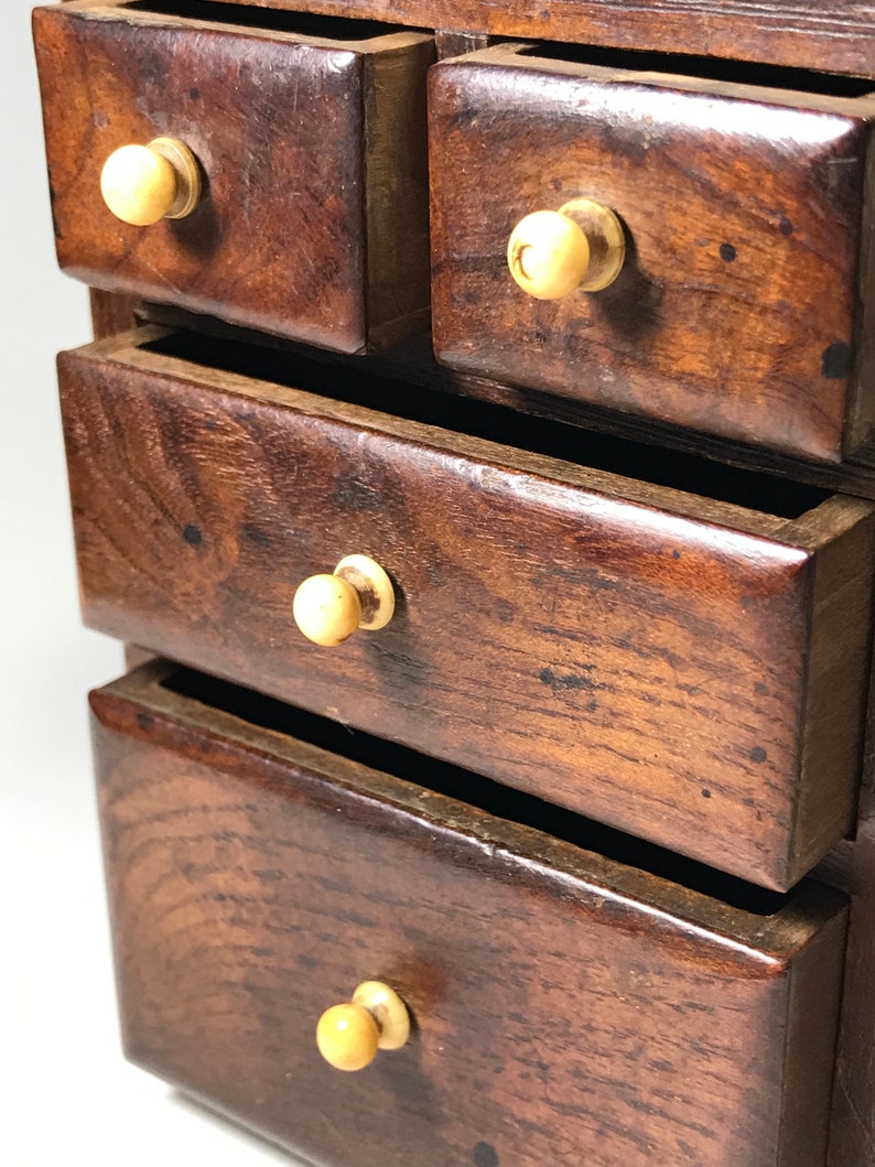May include: A small wooden chest with four drawers. Each drawer has a bone knob and is made of dark wood.