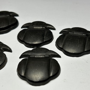 May include: Five black, hinged, decorative boxes with a rounded, scalloped shape. The boxes are made of a smooth, matte material.