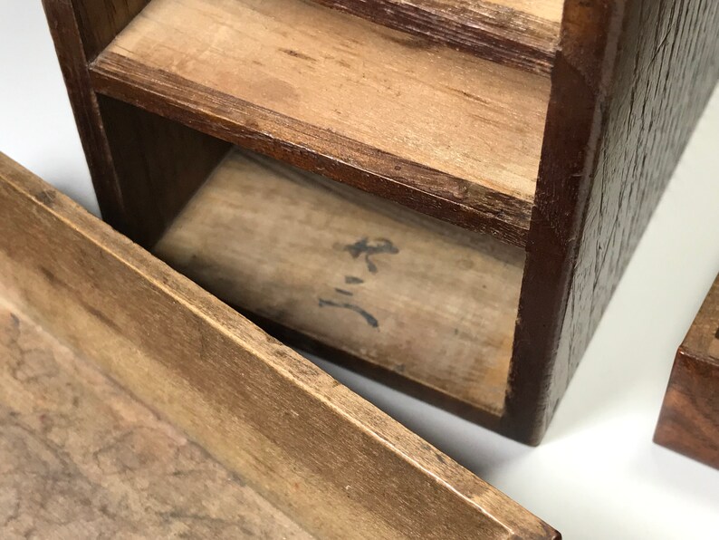 May include: A wooden box with multiple compartments, each with a separate lid. The box is made of dark brown wood and has a natural wood finish. The box is open and the inside is visible. The inside of the box is lined with a light brown wood. The box has a small inscription on the bottom of the box that reads "三".