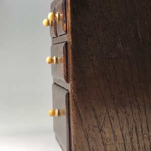 May include: A small wooden chest with four drawers and ivory knobs. The chest is made of dark wood with a natural grain.