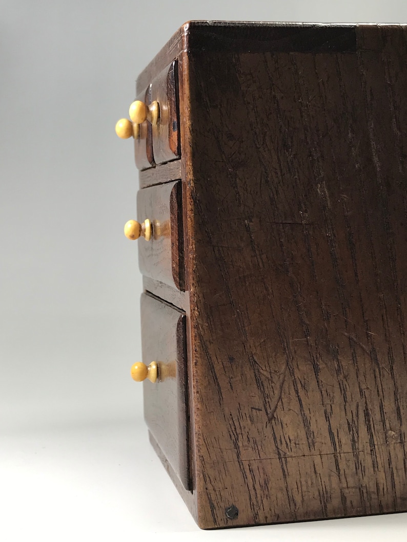 May include: A small wooden chest with four drawers and ivory knobs. The chest is made of dark wood with a natural grain.