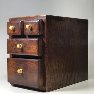 May include: A small wooden chest with four drawers. The chest is made of dark wood and has a simple design. Each drawer has a small, round knob.