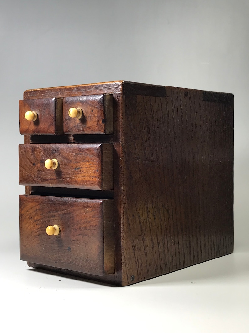May include: A small wooden chest with four drawers. The chest is made of dark wood and has a simple design. Each drawer has a small, round knob.