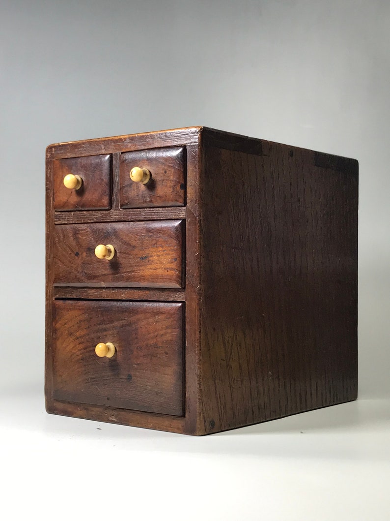 May include: A small wooden chest with five drawers. The drawers have wooden knobs. The chest is dark brown and has a wood grain pattern.
