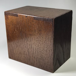 May include: A dark brown wooden box with a simple, rectangular design. The box is made of solid wood and has a smooth, polished finish.