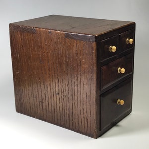 May include: A small wooden box with four drawers. The box is dark brown and has brass knobs on the drawers.