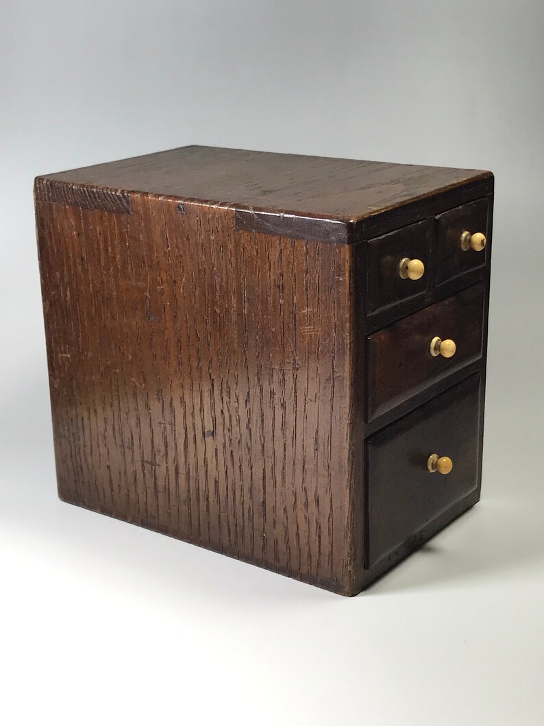 May include: A small wooden box with four drawers. The box is dark brown and has brass knobs on the drawers.