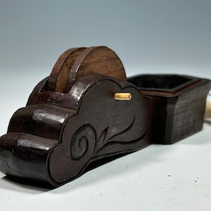 Puede incluir: Un calibrador de marcado de madera marrón oscuro con un cuerpo en forma de nube y un pequeño tintero. El calibrador tiene una rueda y una cuerda con una punta. La madera tiene un acabado pulido y el diseño incluye detalles tallados.