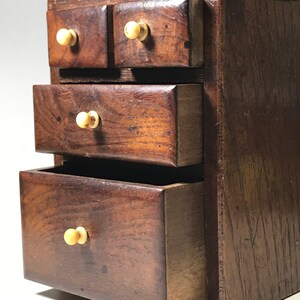 May include: A small wooden chest with four drawers. The drawers have wooden knobs and are made of dark wood. The chest is a decorative piece of furniture.