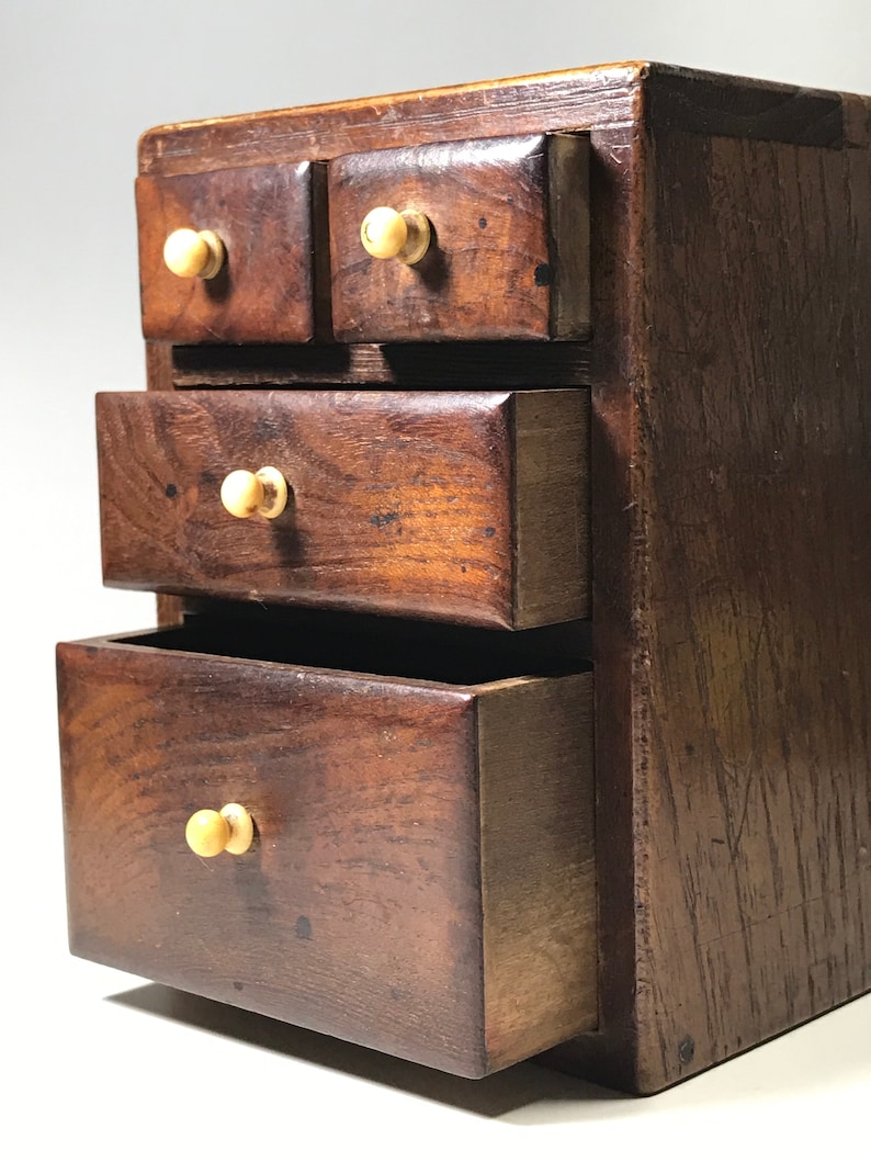 May include: A small wooden chest with four drawers. The drawers have wooden knobs and are made of dark wood. The chest is a decorative piece of furniture.