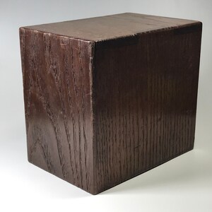 May include: A dark brown wooden box with a smooth, polished finish. The box is rectangular in shape and has a simple, elegant design.