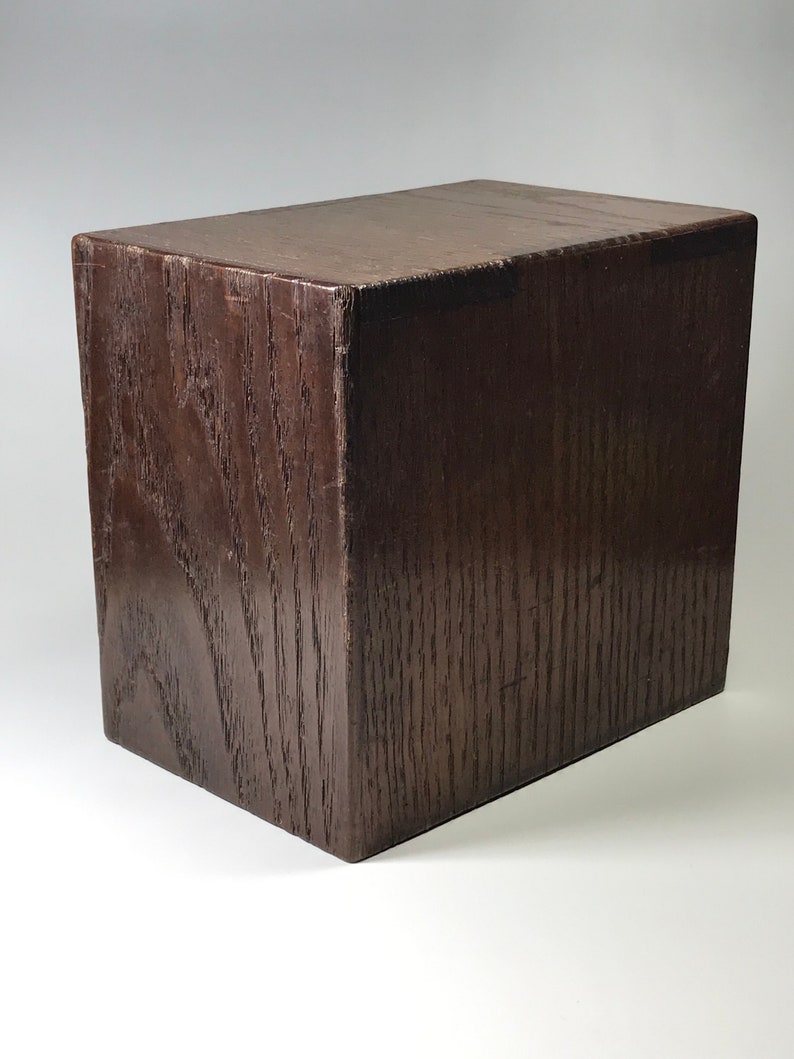 May include: A dark brown wooden box with a smooth, polished finish. The box is rectangular in shape and has a simple, elegant design.