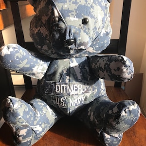 May include: A blue camouflage teddy bear with a name tag that reads "Ditmer U.S. Navy".