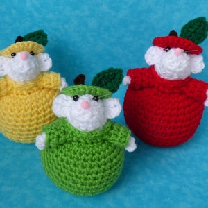 May include: Three crocheted stuffed mice dressed as apples. The mice are wearing yellow, red, and green apple costumes.