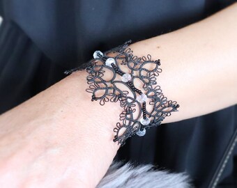 Puede incluir: Un brazalete de encaje negro con cuentas transparentes. El brazalete es delicado e intrincado, con un diseño floral.
